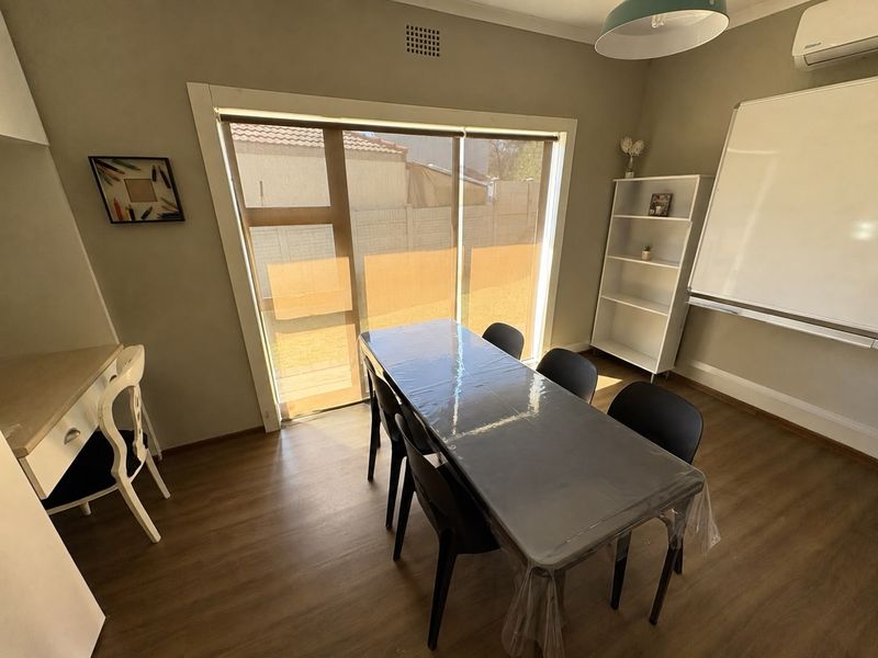 A functional office space featuring laminate flooring, an air conditioning unit, and a large sliding glass door providing natural light.