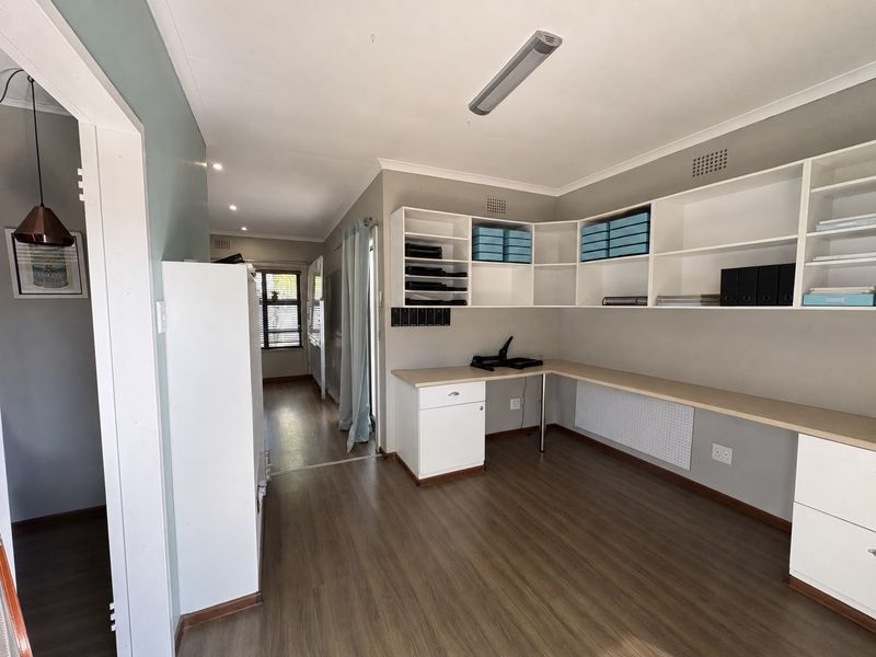 A functional home office featuring extensive built-in desk space and overhead shelving, finished with modern laminate flooring and neutral wall tones.