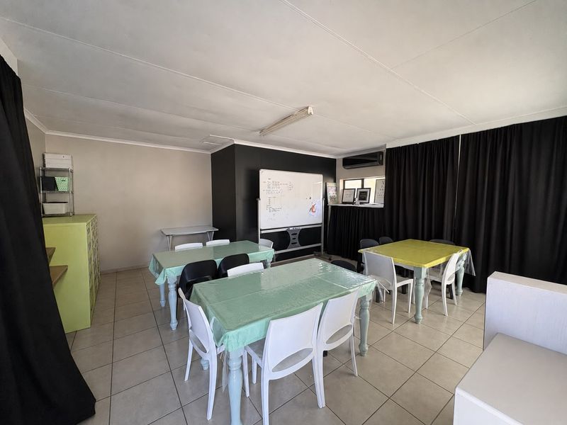 A functional office or multi-purpose room featuring tiled flooring, an air conditioning unit, and overhead lighting, currently set up with multiple tables.