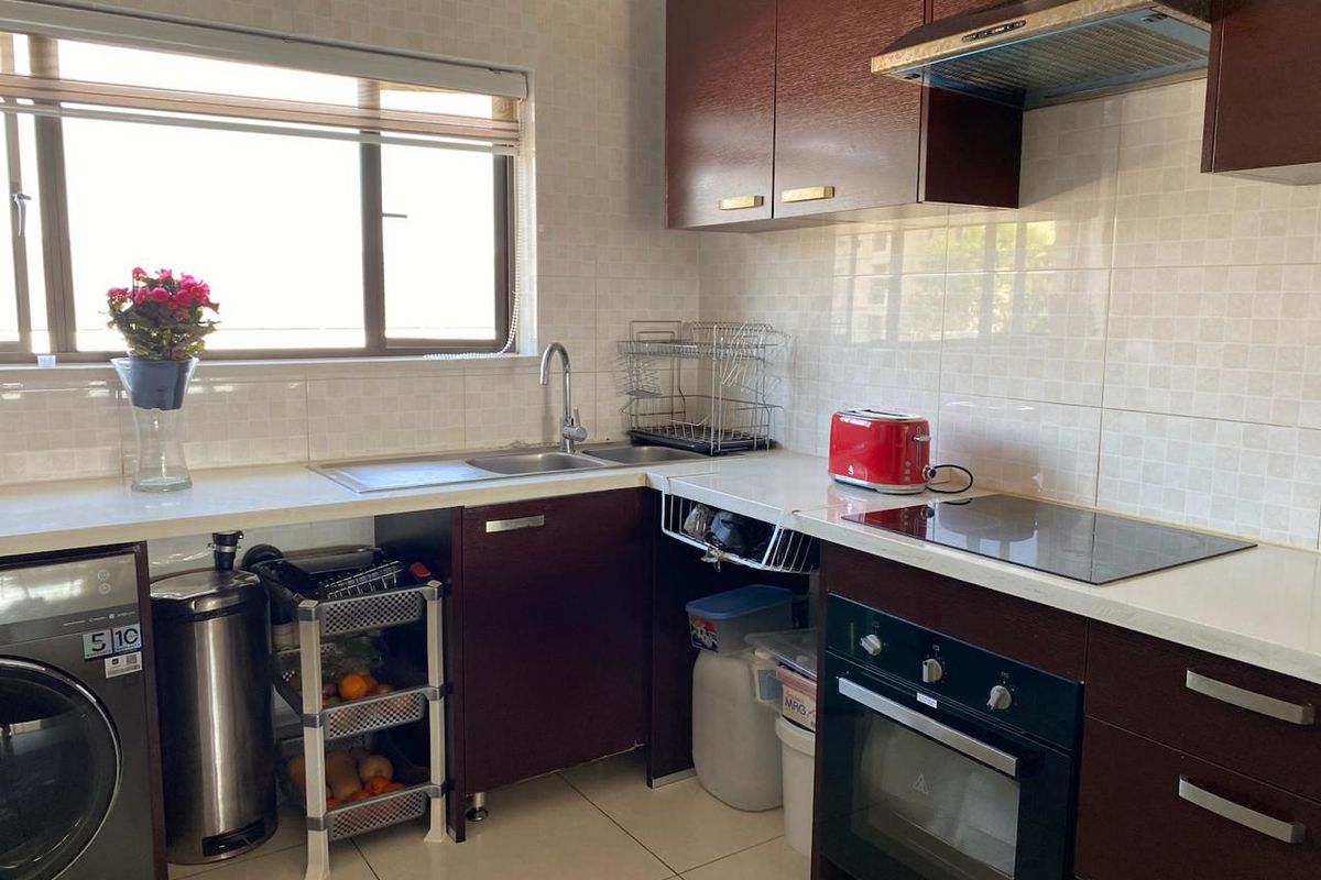 A functional kitchen featuring dark wood cabinetry, light countertops, integrated oven and hob, extractor fan, and tiled finishes with space for laundry appliances.