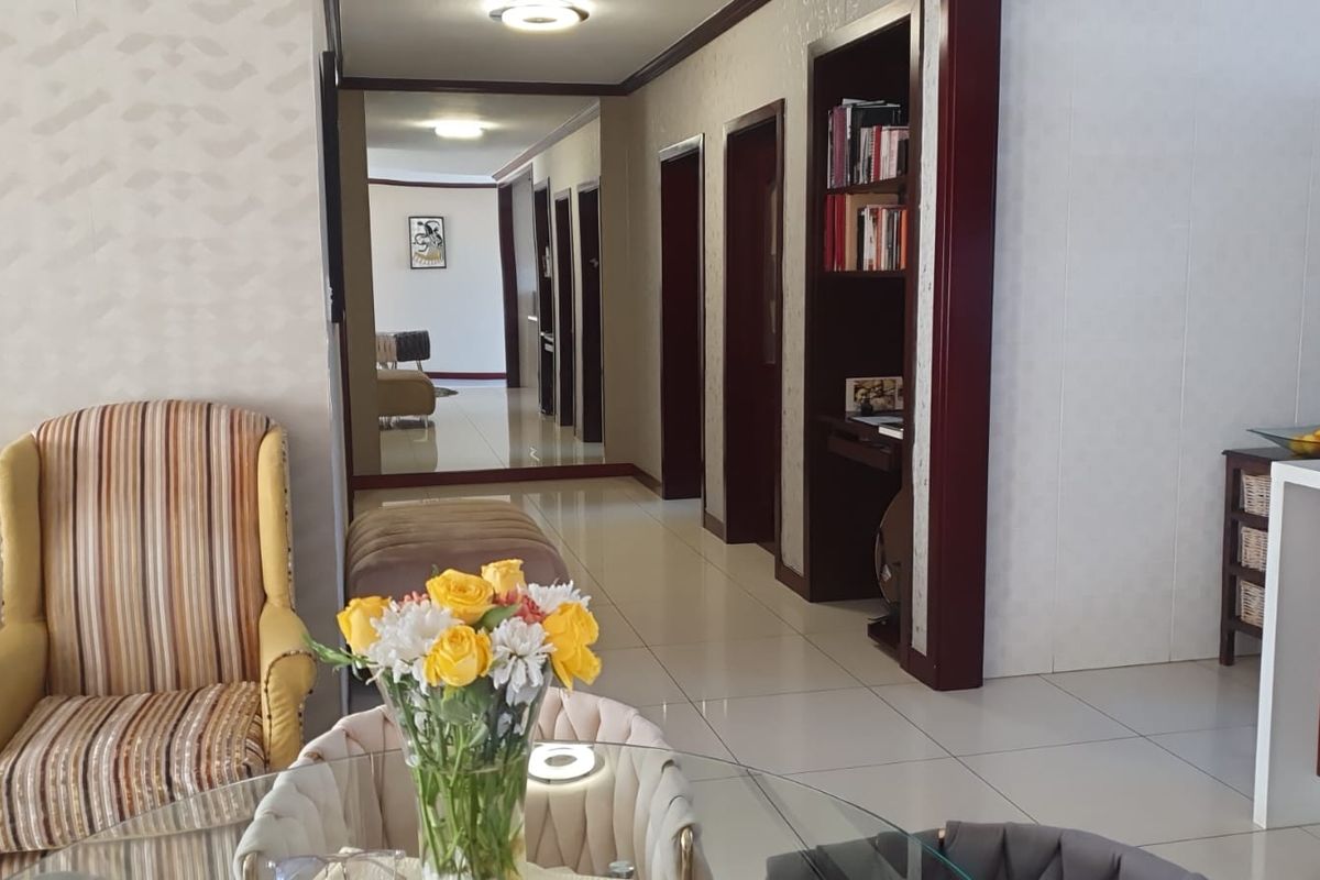 A bright living area featuring tiled flooring, a large mirrored wall, and built-in shelving, leading into a hallway with multiple doorways.