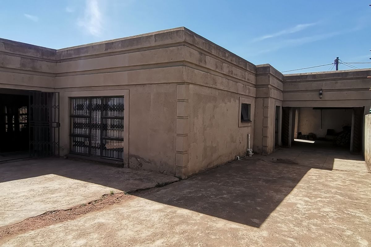 Rear exterior view of the property featuring a concrete driveway, built-in garage, and plastered facade with security gates.