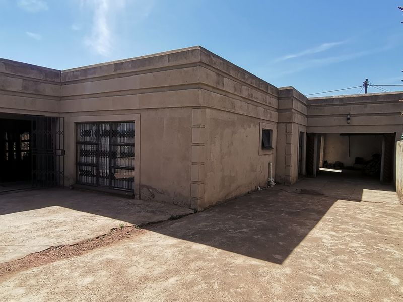 Rear exterior view of the property featuring a concrete driveway, built-in garage, and plastered facade with security gates.