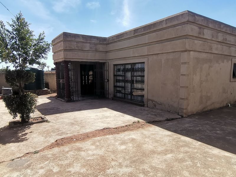 Rear view of the property featuring plastered exterior walls, security gates, and a concrete paved yard area with a water storage tank.
