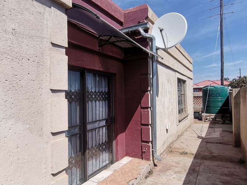 Rear exterior view of the property featuring a paved walkway, security gate, sliding door, and a water storage tank.