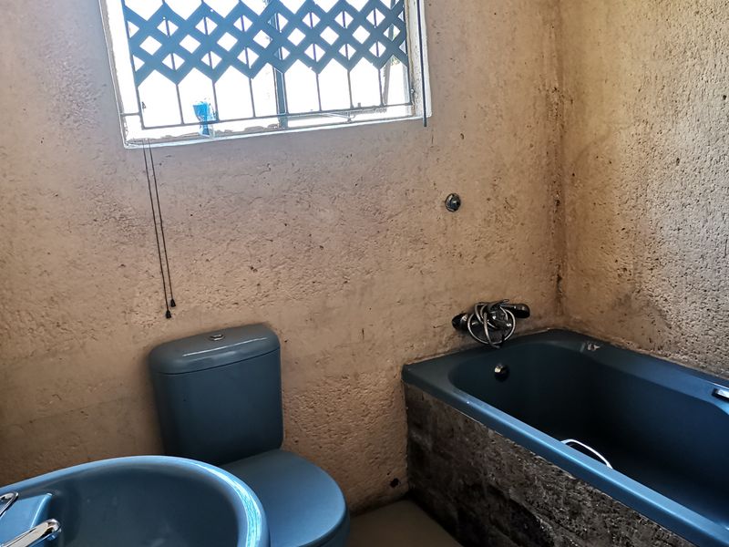 A dated bathroom featuring a blue bathtub, toilet, and pedestal basin with textured walls and security bars on the window.
