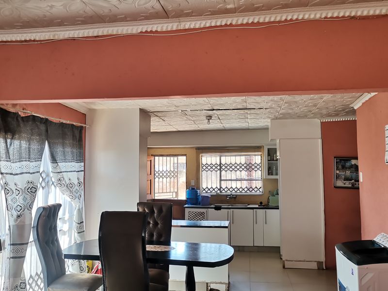 Open plan living and kitchen area featuring tiled floors, decorative ceiling tiles, and functional kitchen cabinetry with security bars on the windows.