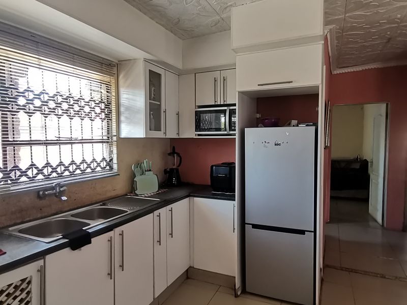 A functional kitchen featuring white built-in cabinetry, a double basin sink, and tiled flooring, offering a practical layout with potential for modern updates.