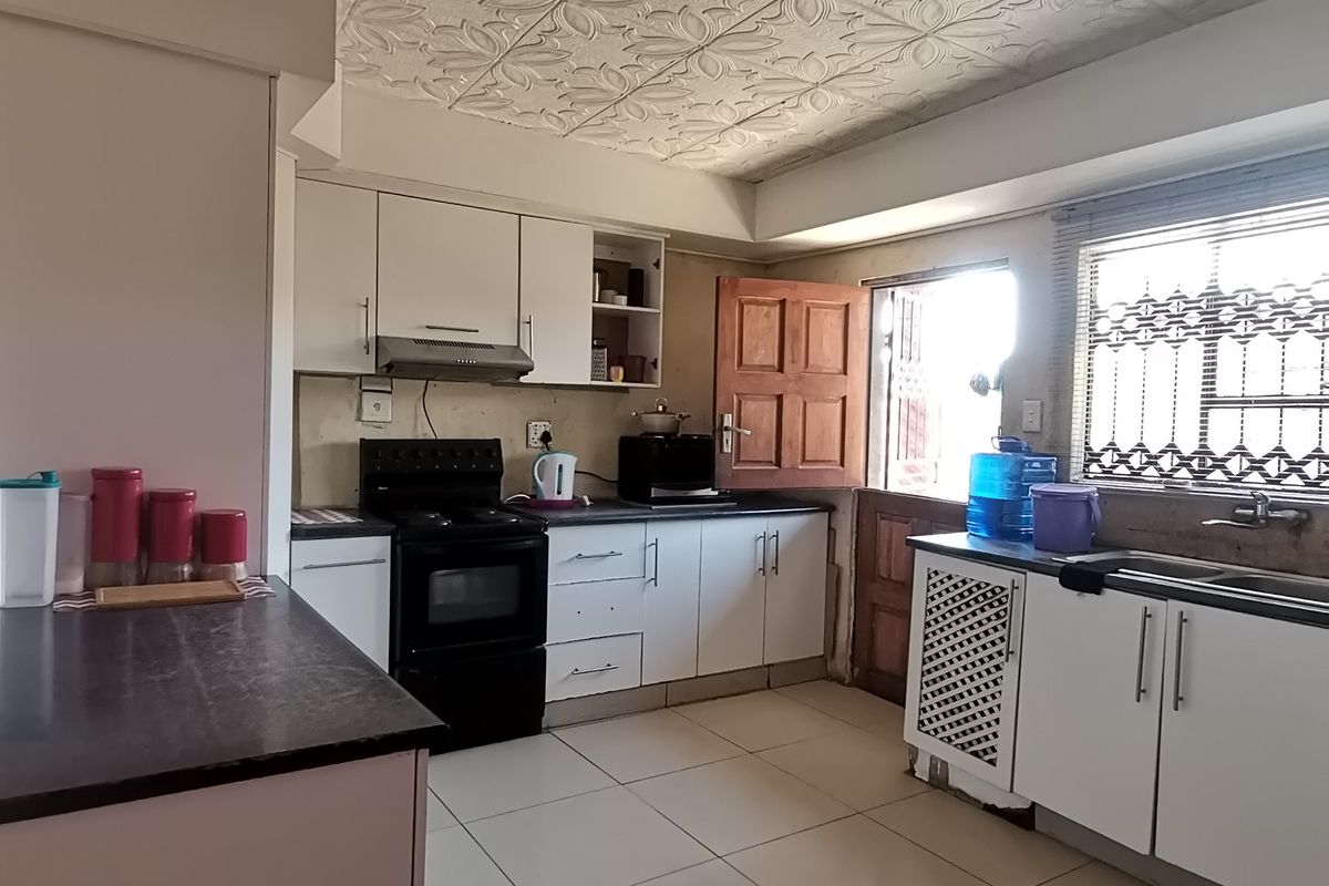 Functional kitchen featuring built-in cabinetry, a stove with extractor fan, double sink, and tiled flooring, offering potential for modern updates.