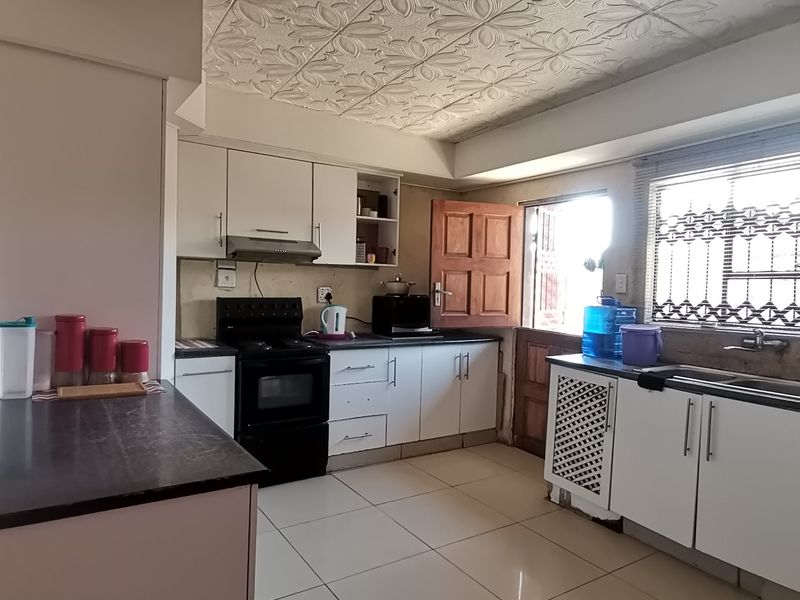 Functional kitchen featuring built-in cabinetry, a stove with extractor fan, double sink, and tiled flooring, offering potential for modern updates.