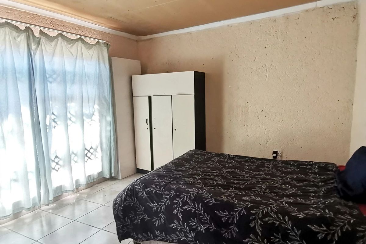 A bedroom featuring tiled flooring, textured walls, and ceiling panels, offering a functional space in need of cosmetic updates.