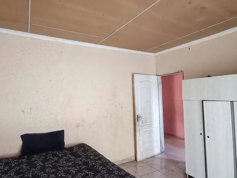 A bedroom featuring tiled flooring and a panel ceiling, currently requiring cosmetic updates to the wall finishes and ceiling panels.