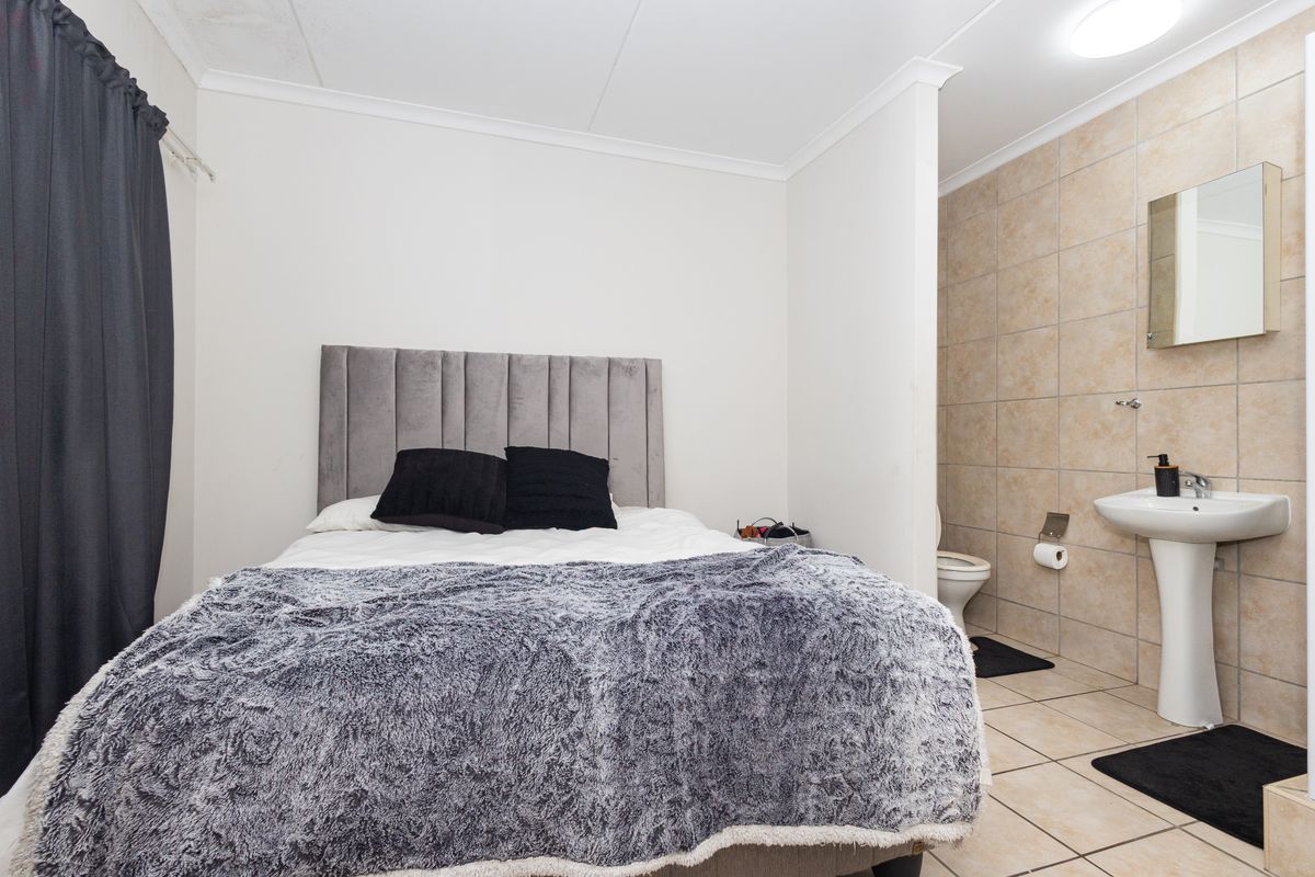Bedroom featuring an open-plan en-suite bathroom with a pedestal basin, tiled walls and flooring, and a neutral interior finish.