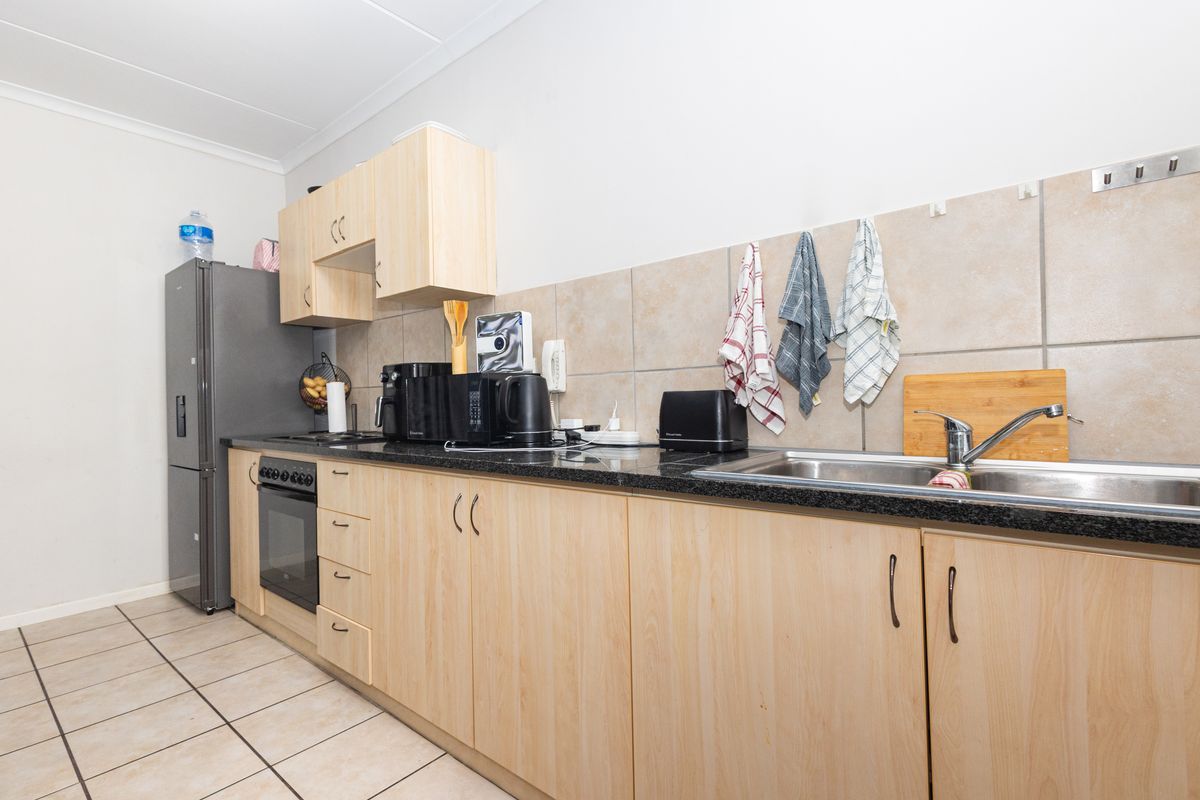 A functional kitchen featuring light wood-finish cabinetry, dark laminate countertops, a stainless steel sink, and tiled flooring with a neutral backsplash.