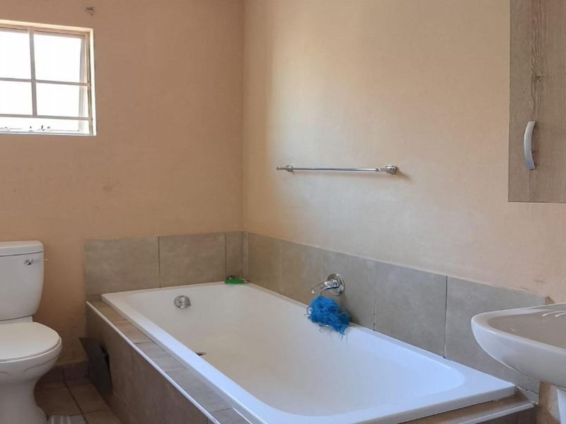 A functional bathroom featuring a standard bathtub, pedestal basin, and toilet with neutral wall finishes and tiled splashbacks.