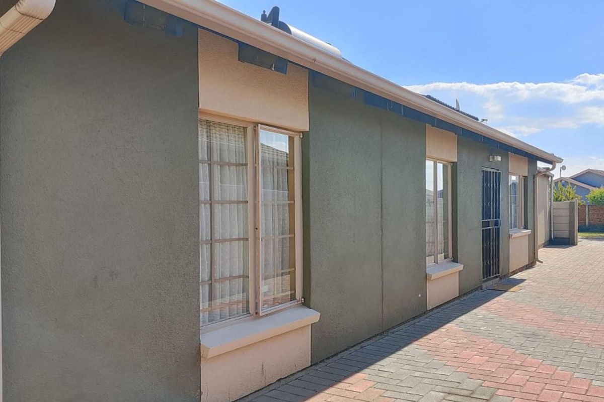A side view of the property featuring paved exterior pathways, secure window frames, and functional guttering along the building facade.