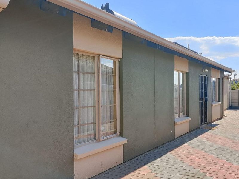 A side view of the property featuring paved exterior pathways, secure window frames, and functional guttering along the building facade.