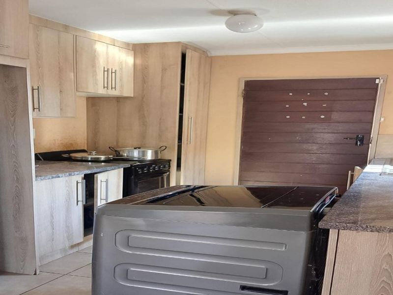 A functional kitchen featuring light wood-look cabinetry, laminate countertops, and tiled flooring, offering a practical layout for daily meal preparation.