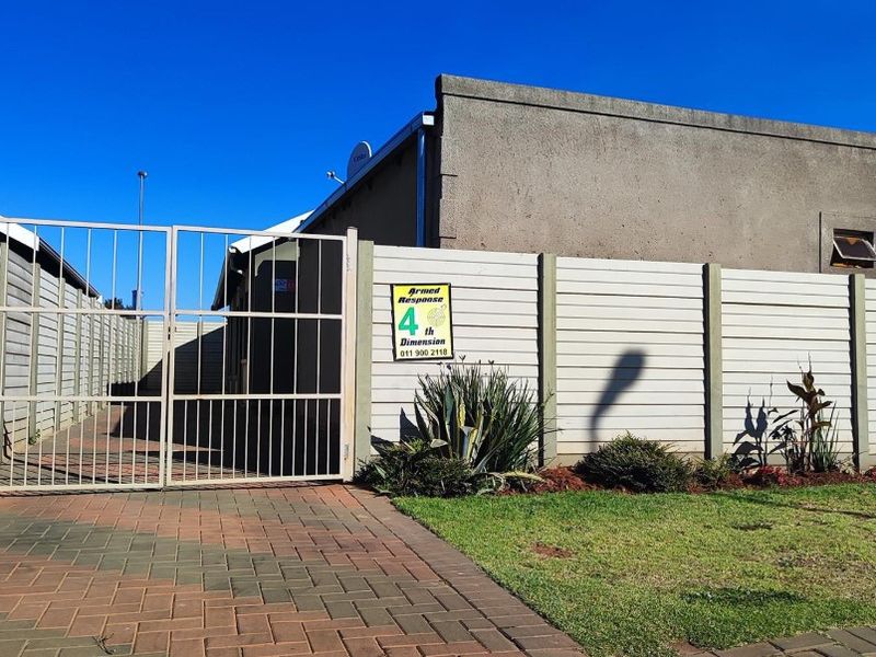 Front exterior view of the property featuring a paved driveway, metal gate, and precast concrete boundary wall.