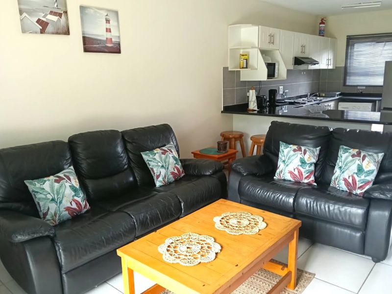 Open-plan living area featuring a functional kitchen with granite countertops, breakfast bar, and tiled flooring, seamlessly connected to the lounge space.