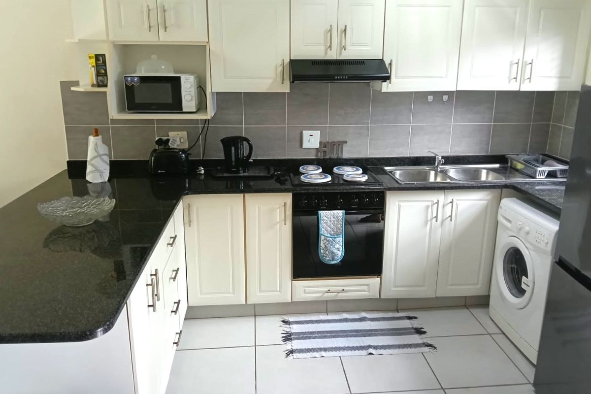 A functional kitchen featuring white cabinetry, dark granite countertops, a built-in oven with hob, extractor fan, and tiled finishes throughout.
