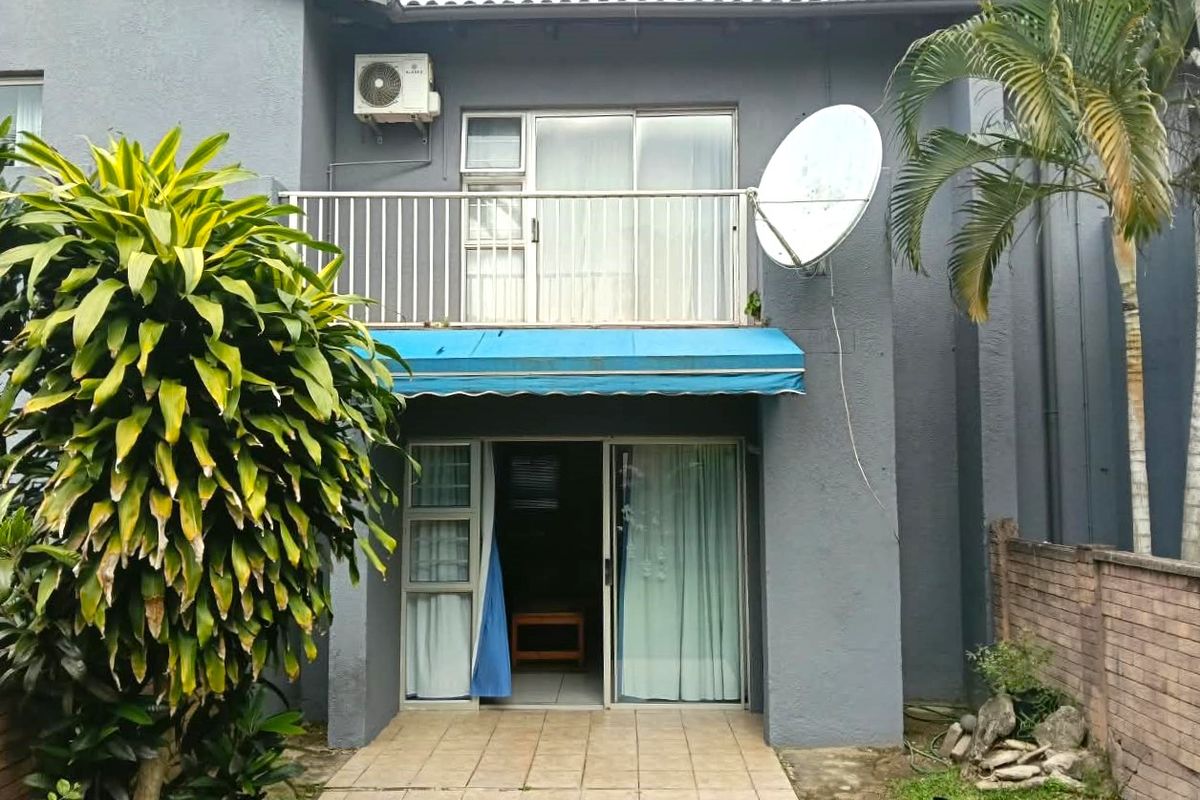Rear view of the townhouse featuring a ground floor tiled patio, a first-floor balcony with sliding doors, and a retractable awning.