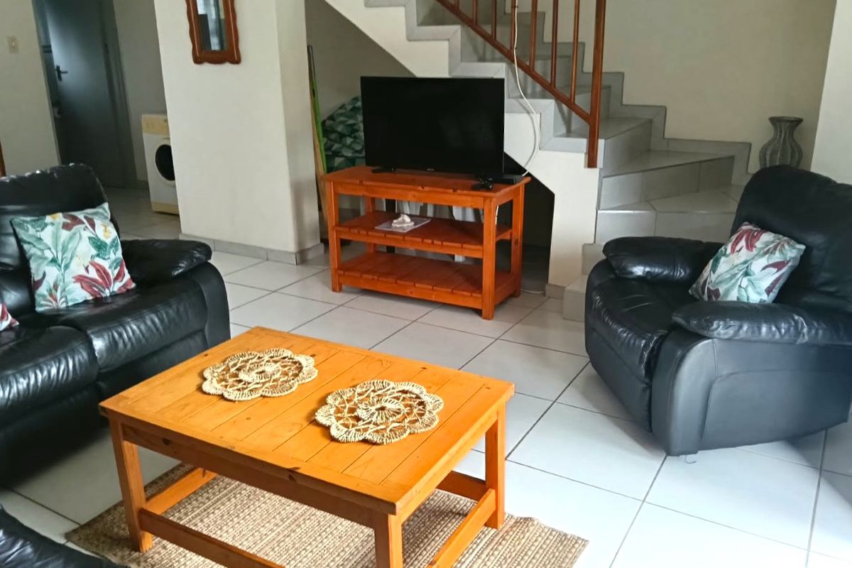 A living room area featuring tiled flooring and an open staircase with a wooden balustrade, providing access to the upper level of the townhouse.