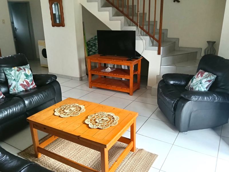 A living room area featuring tiled flooring and an open staircase with a wooden balustrade, providing access to the upper level of the townhouse.
