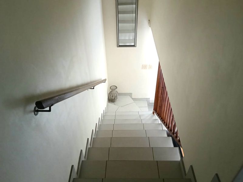 A clean, tiled staircase featuring a wooden handrail and a wooden balustrade, providing a simple and functional transition between levels.