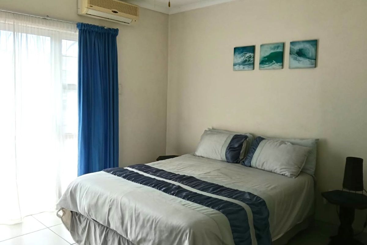 A functional bedroom featuring tiled flooring, a wall-mounted air conditioning unit, and a sliding glass door providing natural light.