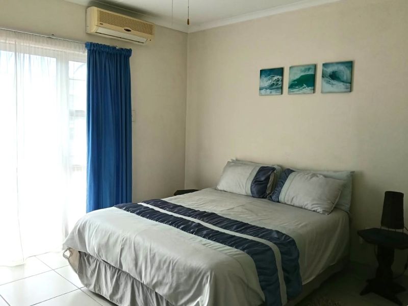 A functional bedroom featuring tiled flooring, a wall-mounted air conditioning unit, and a sliding glass door providing natural light.