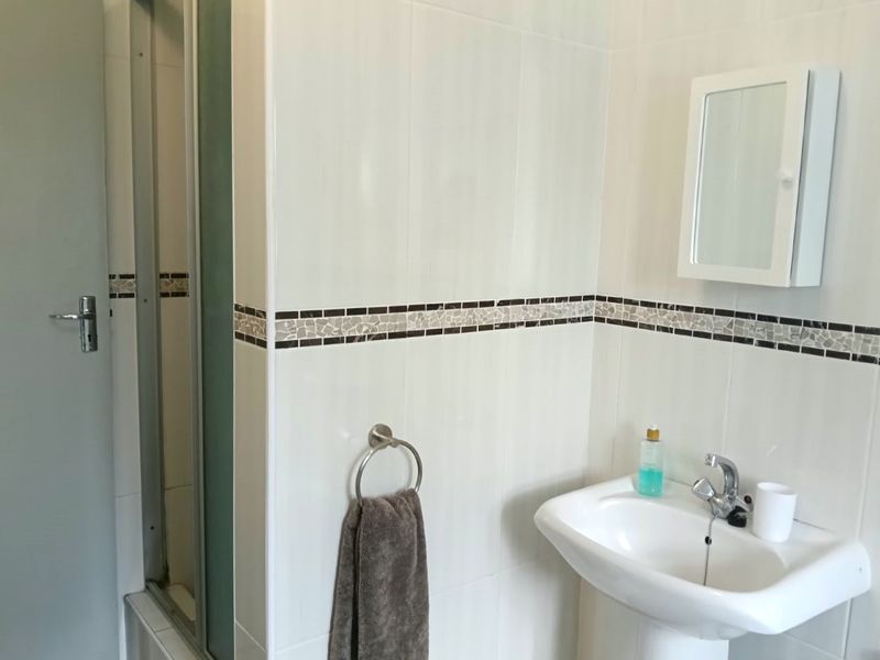 A functional bathroom featuring a pedestal basin, shower enclosure, and wall-mounted medicine cabinet with decorative tiled accents.