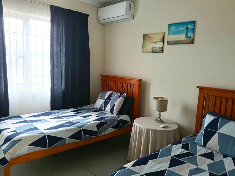 A functional bedroom featuring tiled flooring, a wall-mounted split-system air conditioner, and a window fitted with security bars.