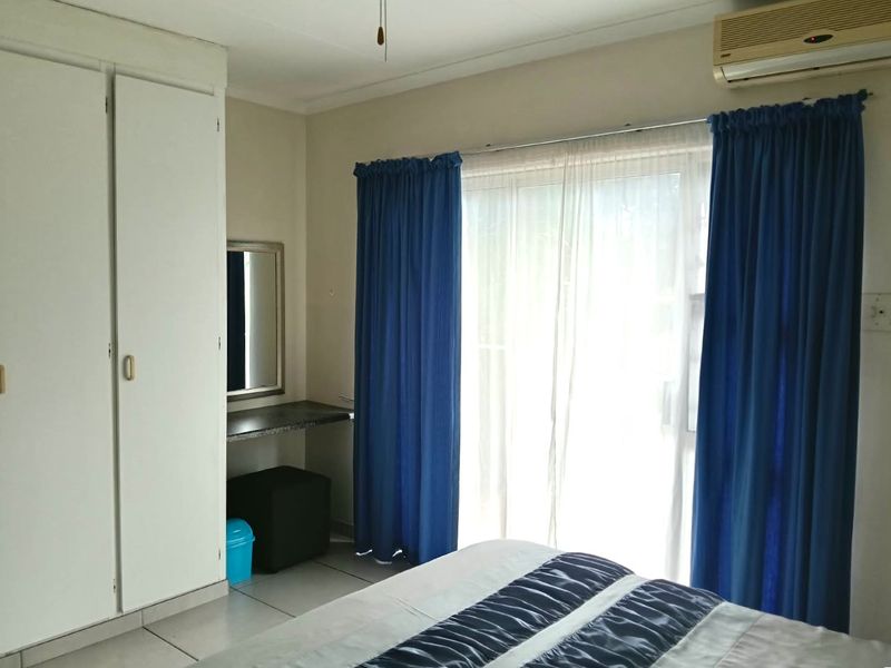 A bedroom featuring tiled flooring, built-in cupboards, a vanity area, and a wall-mounted air conditioning unit with access to a sliding glass door.