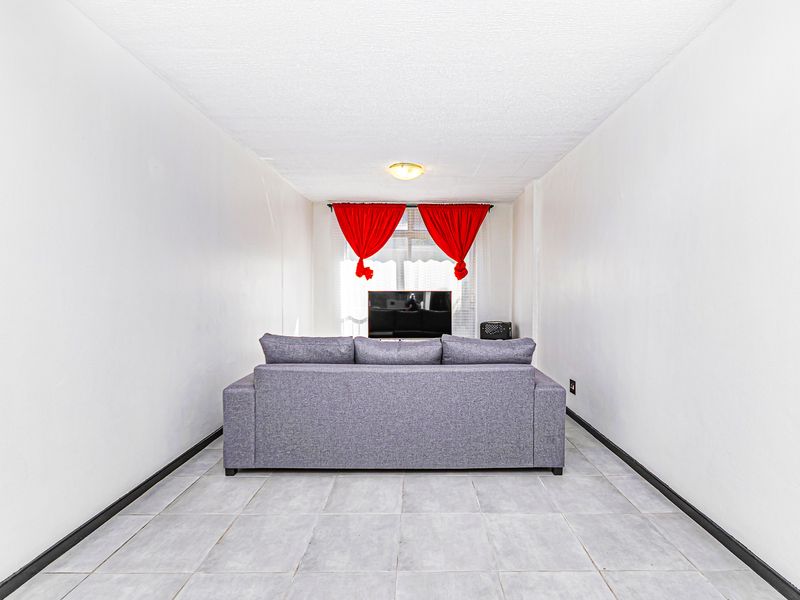 A simple living room featuring tiled flooring, neutral walls, and a central ceiling light fixture, providing a functional and straightforward living space.