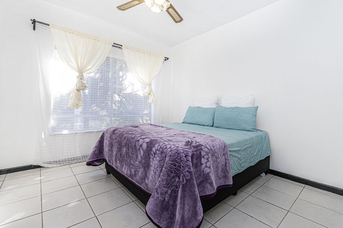 A bright bedroom featuring neutral tiled flooring and a ceiling fan, offering a clean and functional space.