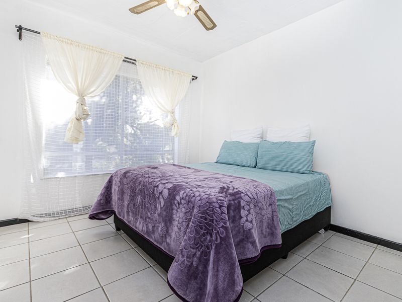 A bright bedroom featuring neutral tiled flooring and a ceiling fan, offering a clean and functional space.