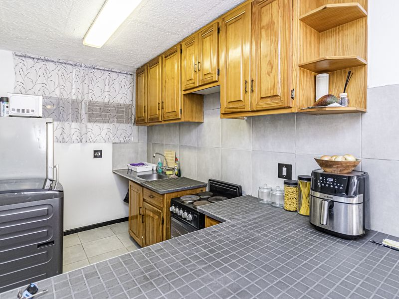 A functional kitchen featuring wooden cabinetry, tiled countertops, a tiled backsplash, and a freestanding stove, offering a practical layout for daily meal preparation.