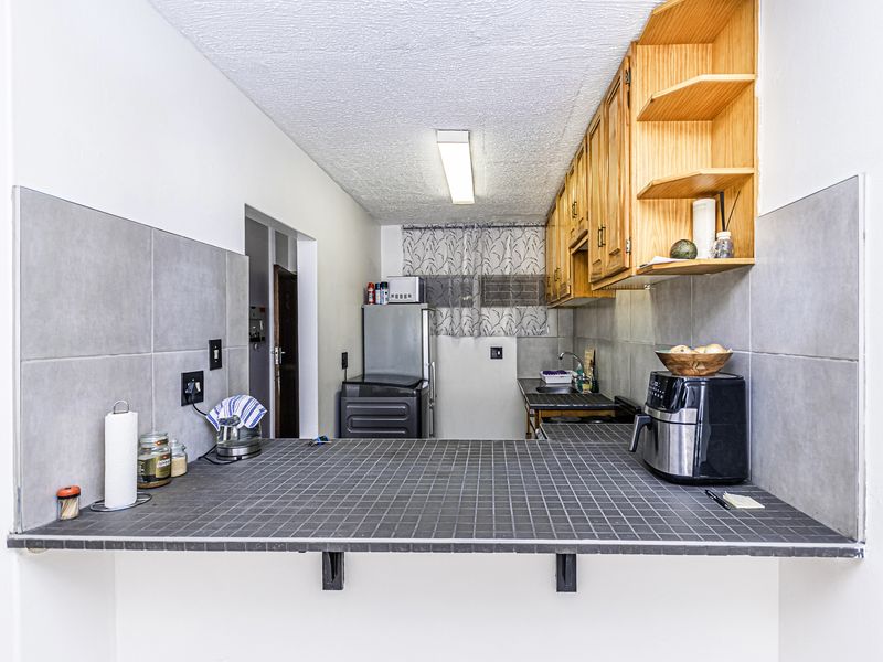 A functional kitchen featuring wooden cabinetry, open shelving, a tiled breakfast bar, and a tiled splashback, offering a practical layout for daily use.