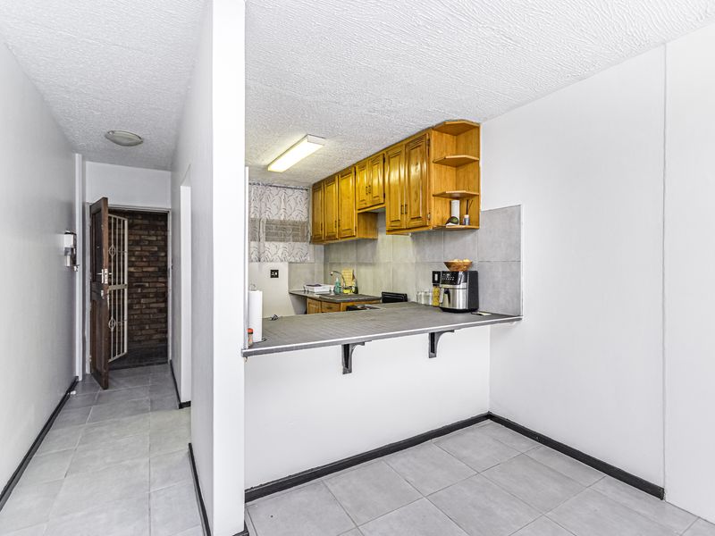 Open plan kitchen area featuring wooden cabinetry, a breakfast bar, and tiled flooring, adjacent to a hallway with a security gate entrance.