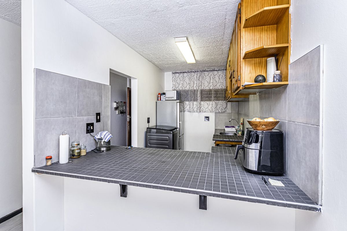A functional kitchen featuring a tiled breakfast bar, wooden cabinetry, and neutral wall tiling, offering a practical layout for daily meal preparation.
