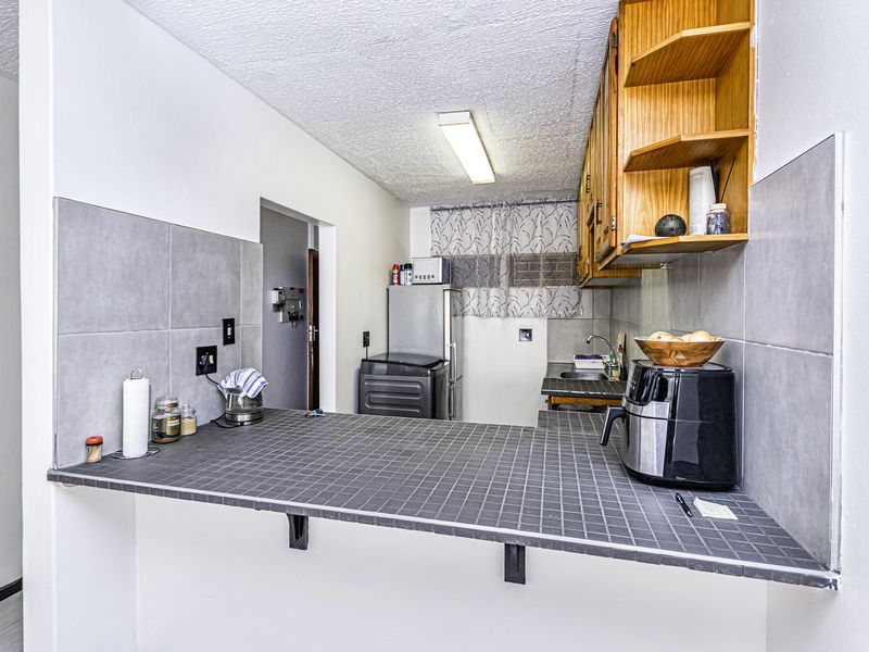 A functional kitchen featuring a tiled breakfast bar, wooden cabinetry, and neutral wall tiling, offering a practical layout for daily meal preparation.