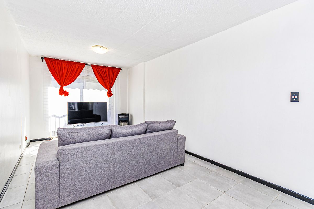 A simple living room featuring tiled flooring, a ceiling light fixture, and a sliding glass door leading to an outdoor area.