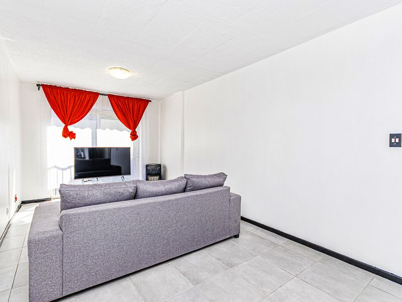 A simple living room featuring tiled flooring, a ceiling light fixture, and a sliding glass door leading to an outdoor area.