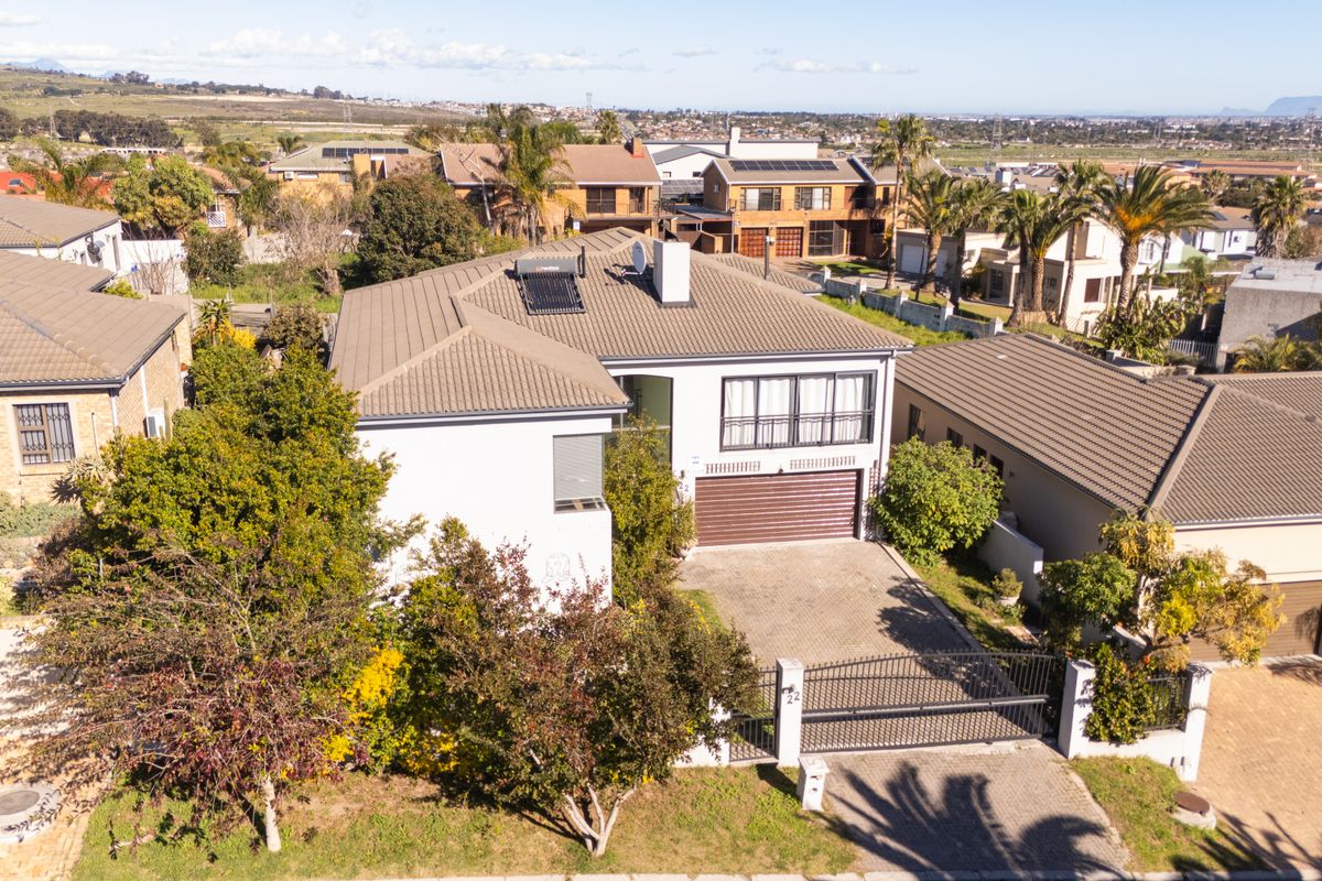 Aerial view of a residential property featuring a tiled roof with solar heating, a paved driveway, and secure gated access.