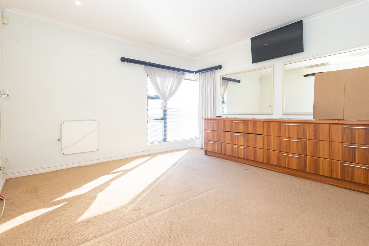 A bedroom featuring built-in wooden cabinetry, wall-mounted heating, and carpet flooring, offering a functional space with potential for cosmetic updates.