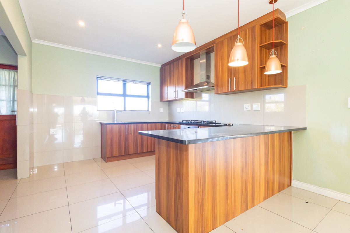 Modern kitchen featuring wood-finish cabinetry, granite countertops, gas hob, extractor fan, and tiled flooring in an open-plan layout.