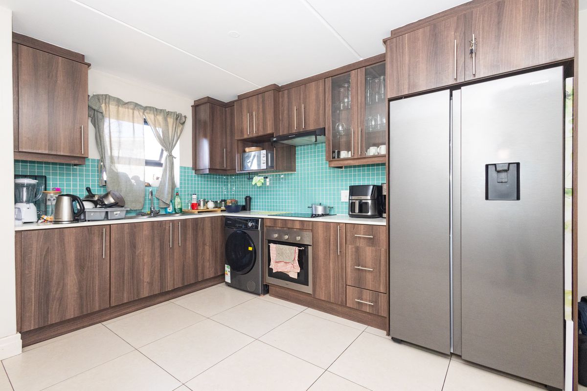 A functional kitchen featuring dark wood-look cabinetry, a vibrant teal tiled backsplash, built-in oven, and integrated hob with extractor fan.
