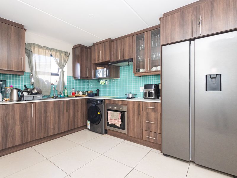 A functional kitchen featuring dark wood-look cabinetry, a vibrant teal tiled backsplash, built-in oven, and integrated hob with extractor fan.