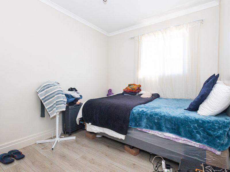 A standard bedroom featuring light-toned laminate flooring, neutral wall finishes, and a window with natural light.